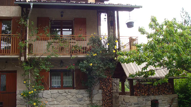 Vue d'une maison en pierre et bois sur trois étages, balcon métallique, cour intérieure, abri de jardin, végétation
