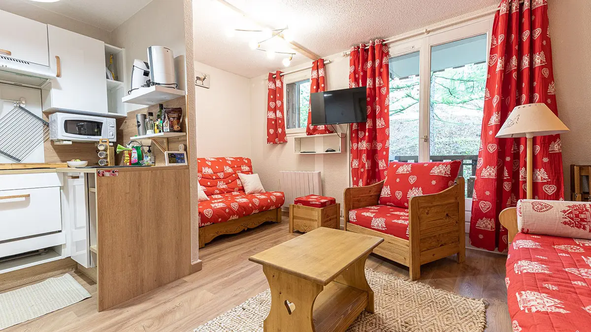 Bright studio apartment living room with sofa and armchairs, coffee table, equipped kitchenette, wooden furniture, windows