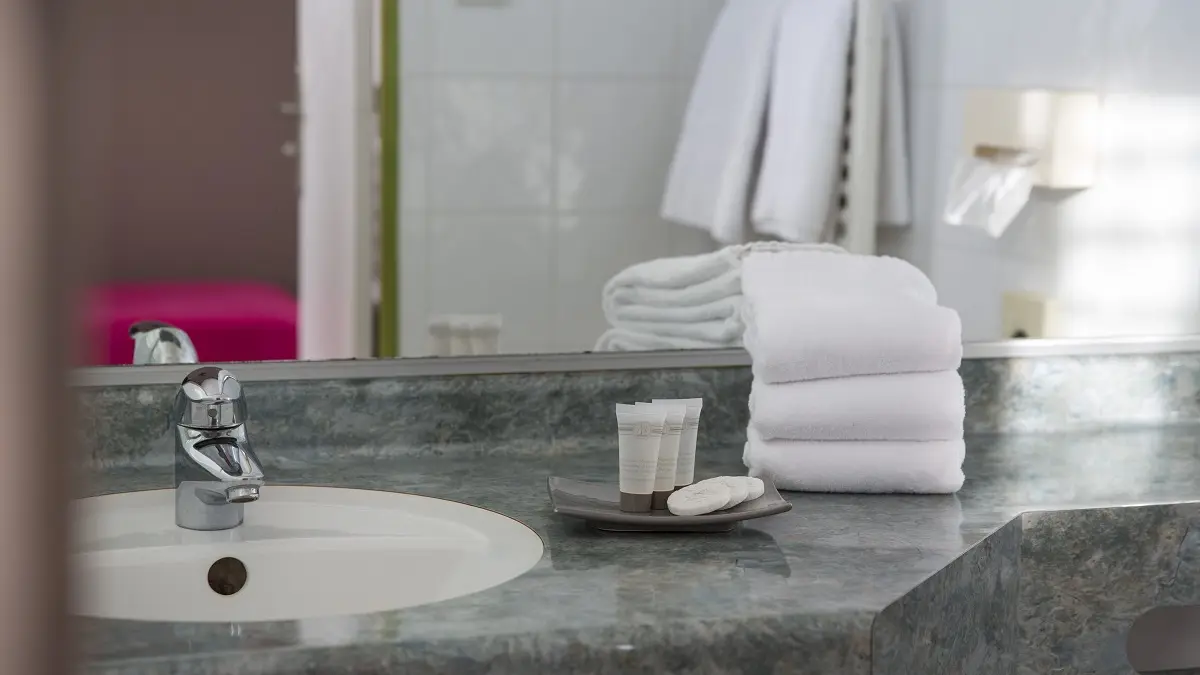 Salle de bain en marbre gris avec un lavabo blanc et quelques serviettes soigneusement pliées.