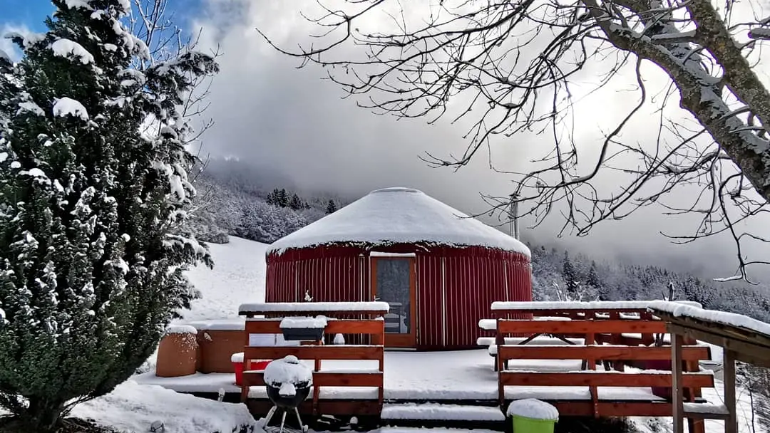 Une yourte rouge avec sa terrasse dans un paysage enneigée.