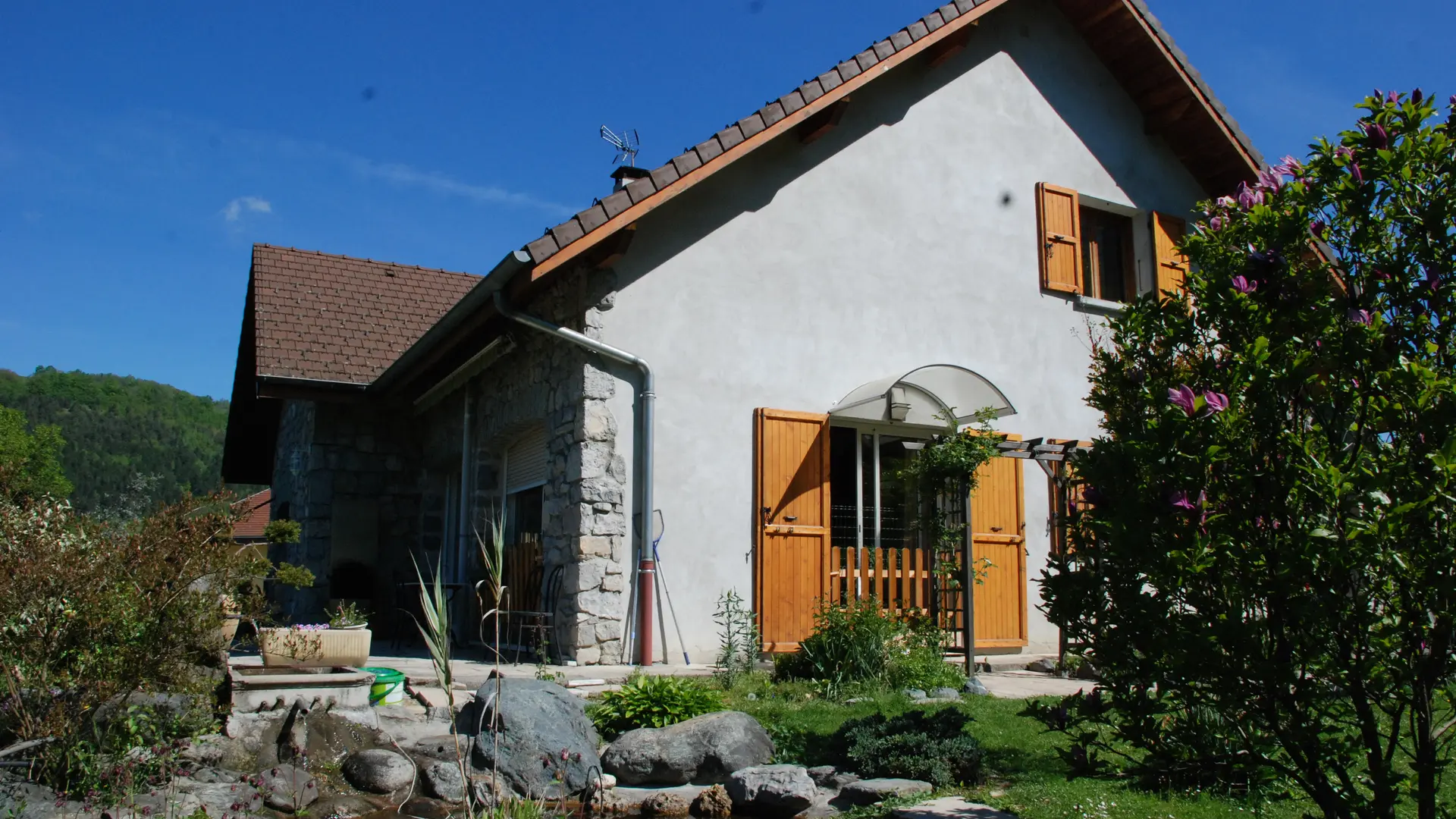 C'est une maison à un étage avec un toit à deux pans. Les murs extérieurs sont en pierre et les ouvertures sont protégées par des volets.