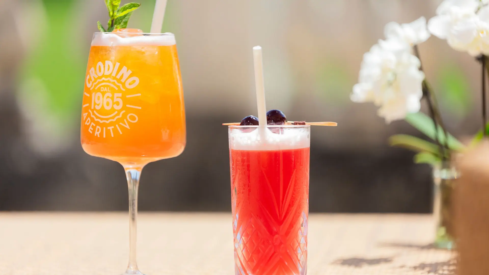 Deux cocktails colorés garnis d'une paille, l'une dans un verre à pied et l'autre dans un verre droit plus petit.