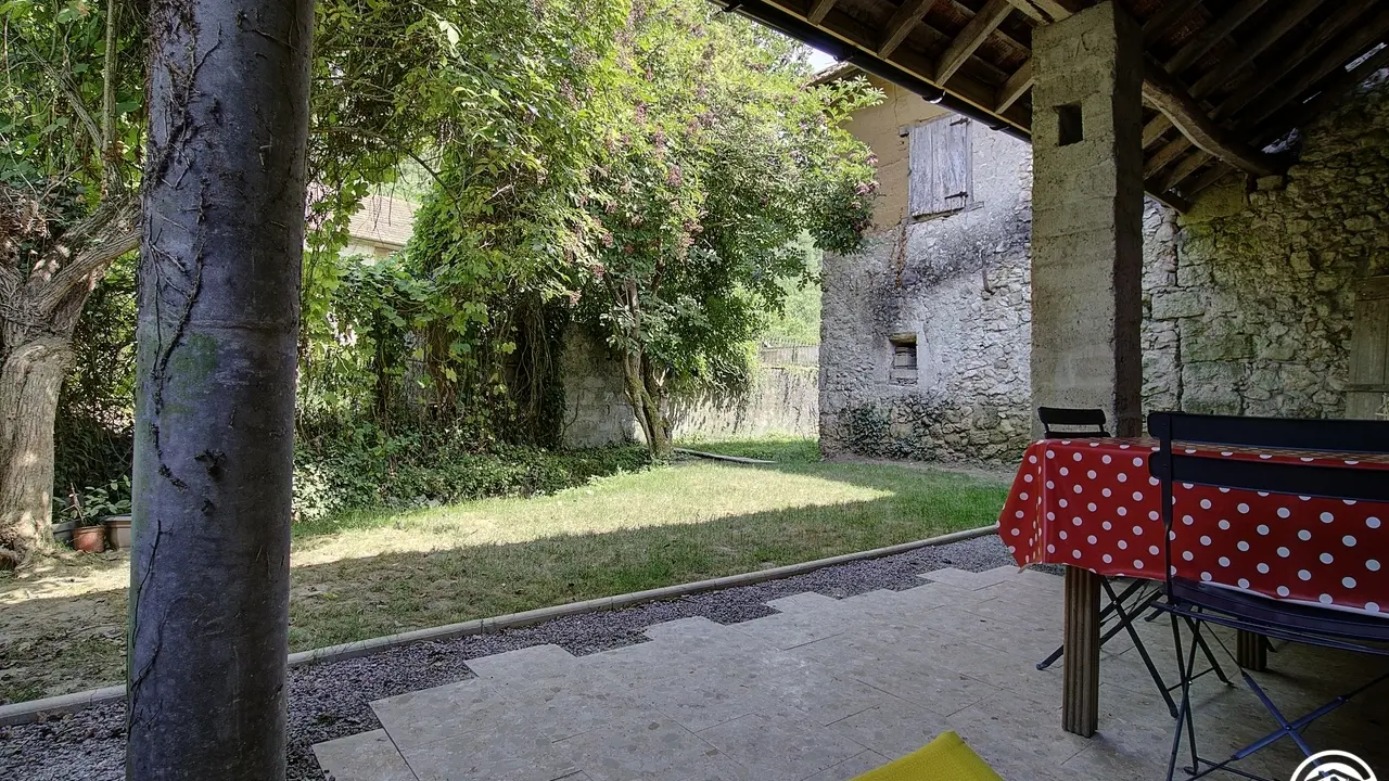 Vue de la terrasse couverte, son petit jardin ombragé, bordé par la petite rivière