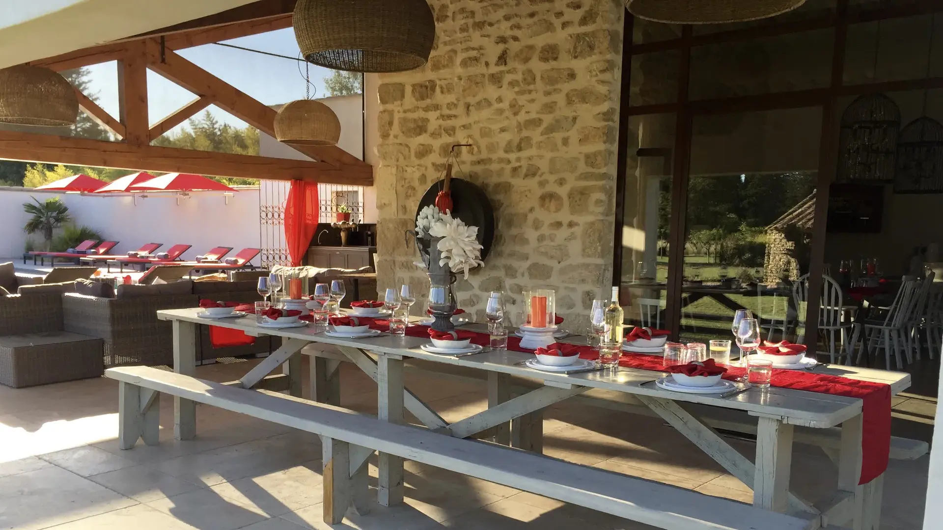 Salle à manger extérieure sous pergola, grande table dressée et espace lounge.