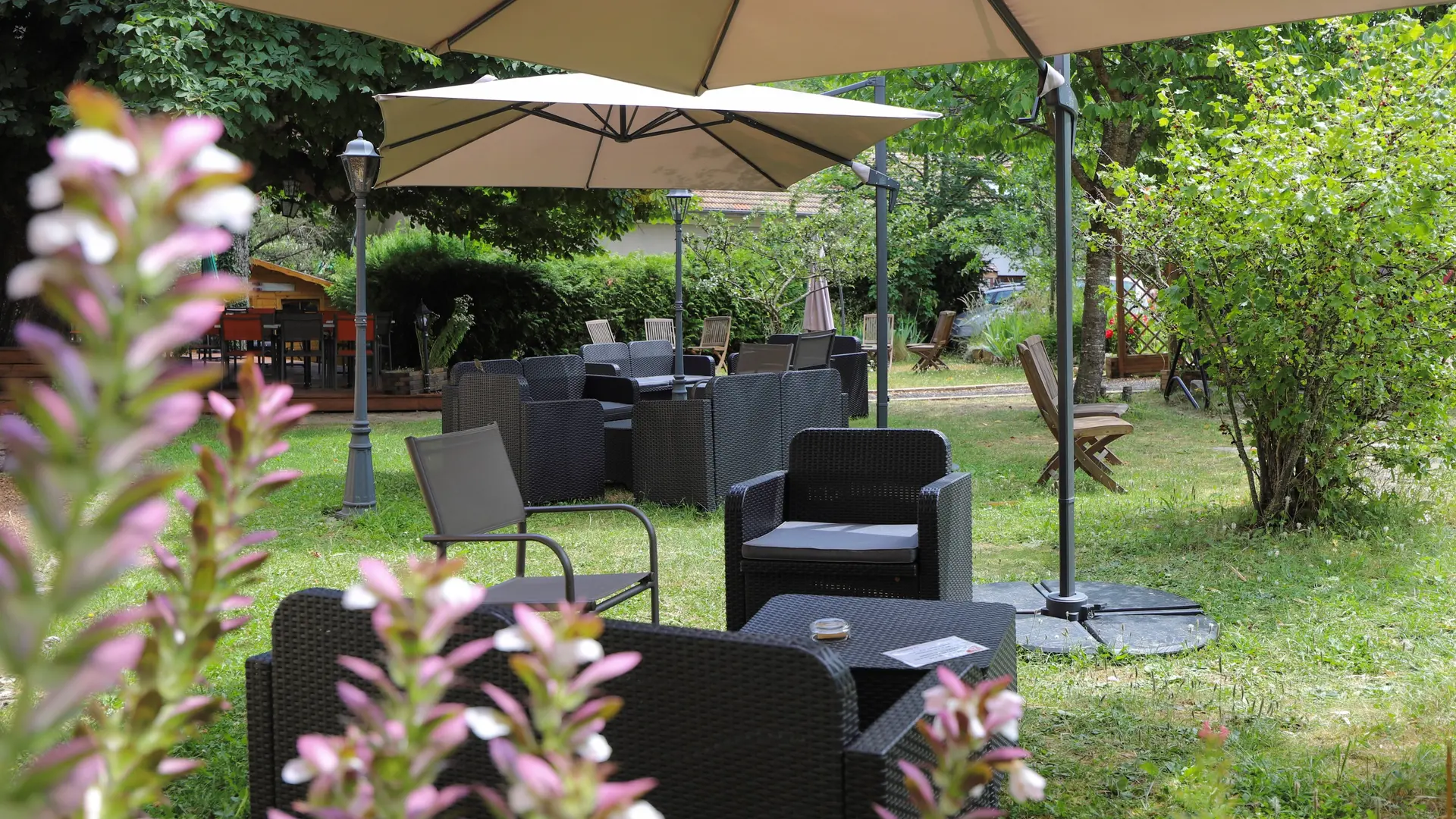 Salons de jardin installés sur la pelouse, abrités par de grands parasols et entourés d’arbres
