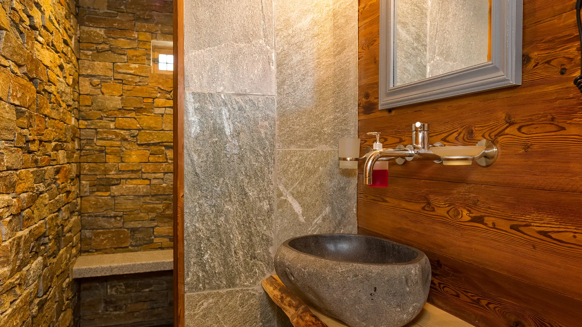 Salle de bains avec vasque en pierre, sous-vasque en bois, murs en pierre de la douche