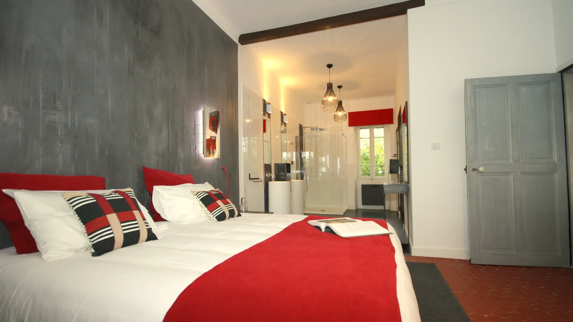 Chambre moderne gris et rouge, lits jumeaux et salle de bain attenante.