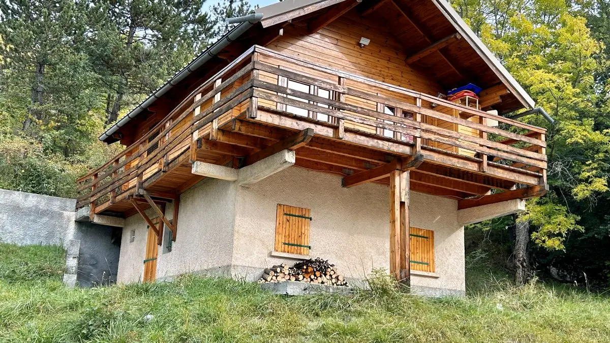 Front view of the two-storey stone and timber cottage, timber terrace and garden, vegetation