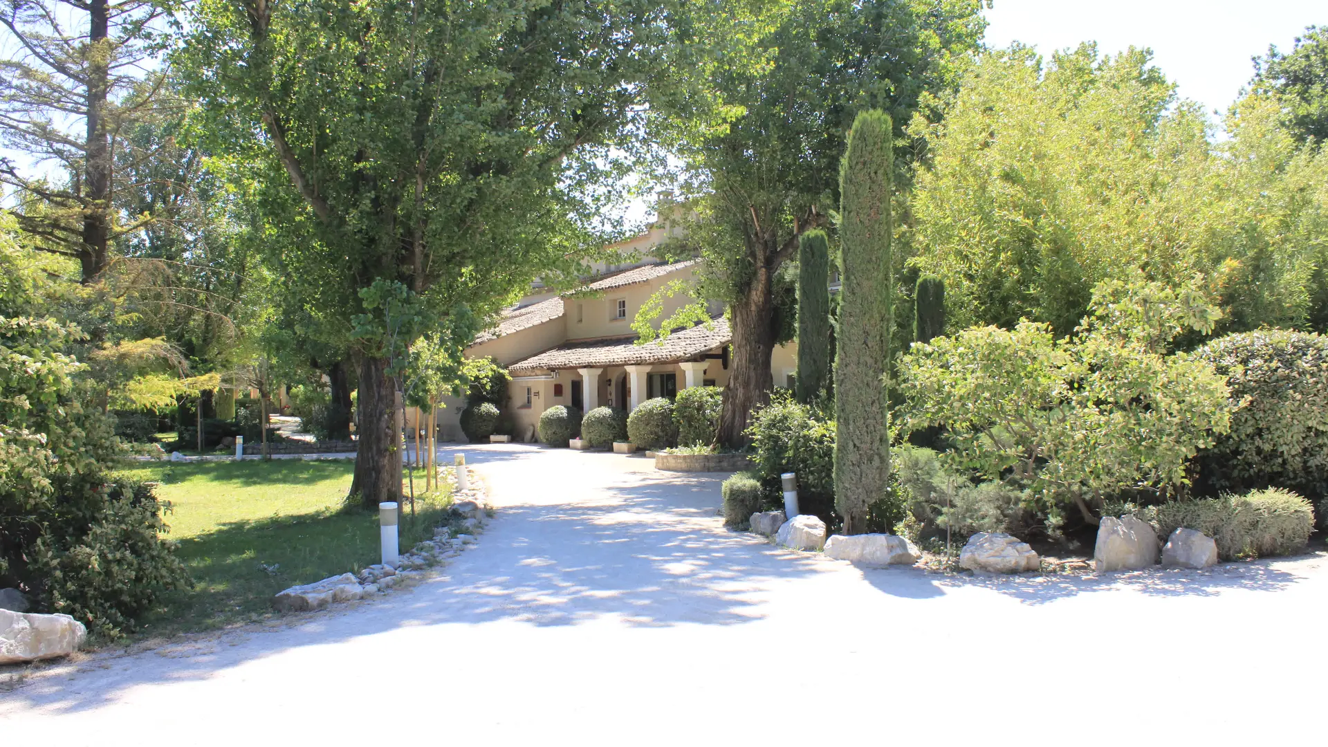 Une grande bastide provençale nichée au cœur d’un écrin de verdure, accessible par une allée ombragée.