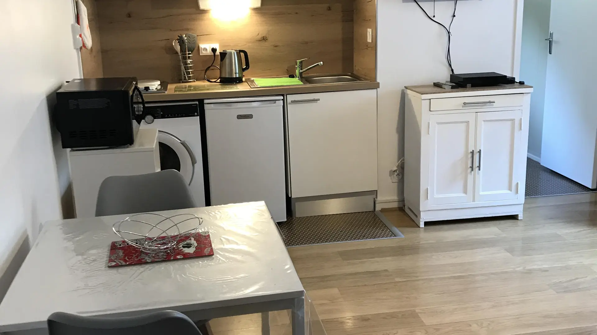 C'est une petite cuisine équipée d'un plan de travail avec un évier, des plaques de cuisson et un four micro-ondes. Il y a également un réfrigérateur, un lave-linge et des rangements muraux.