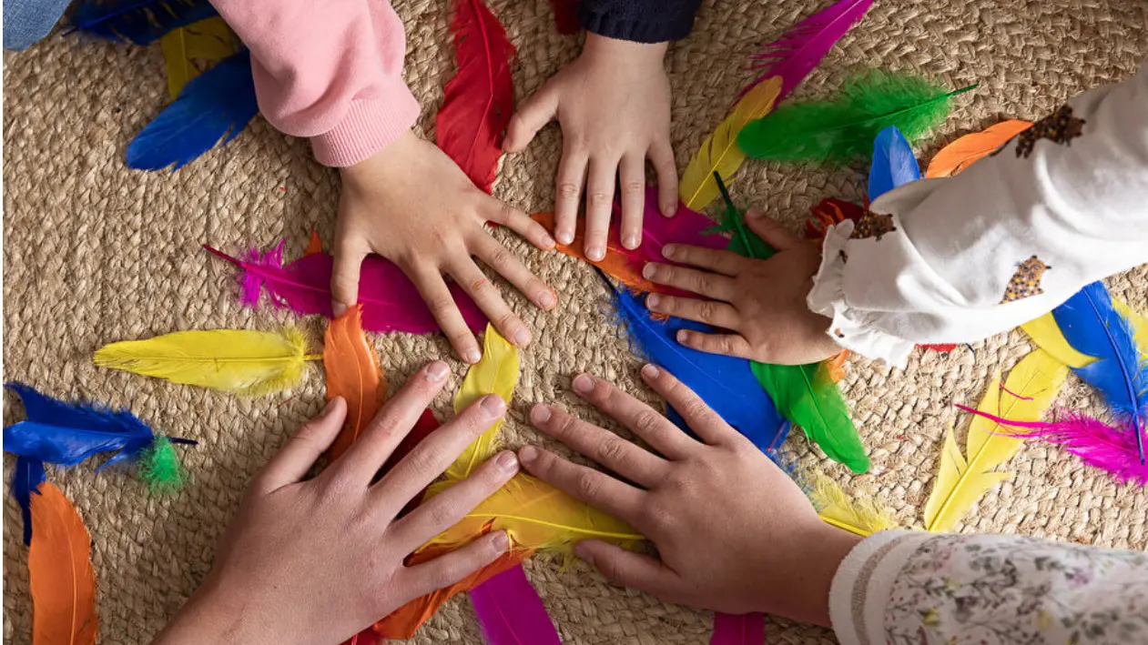 Différentes mains d'enfants et d'adulte formant un cercle sur des plumes colorées.
