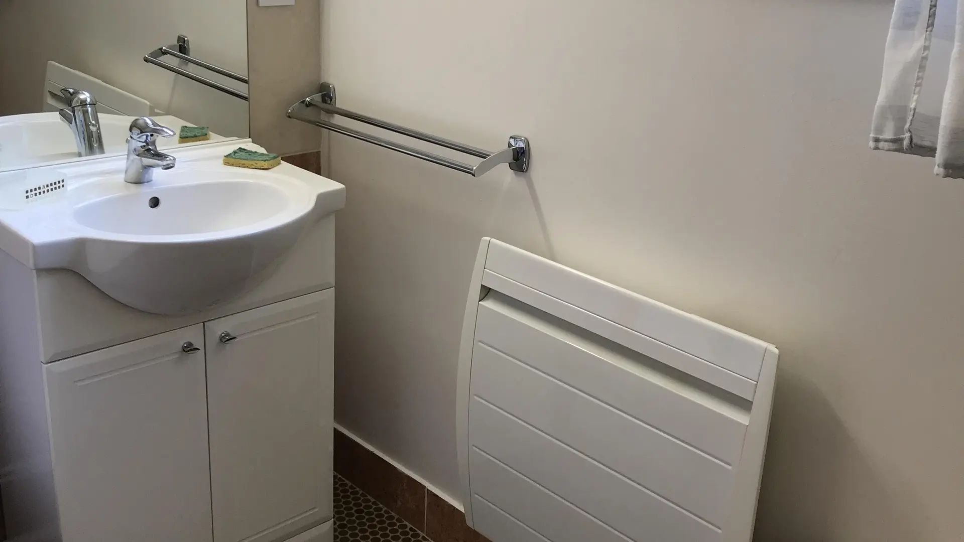 C'est une salle d'eau avec un lavabo avec un meuble sous vasque, un miroir et un panier à linge.