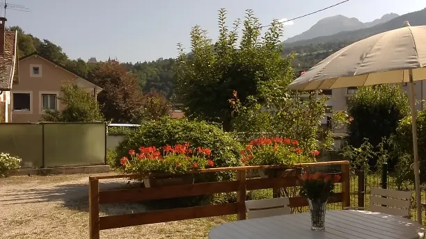 La terrasse, aménagée avec du mobilier de jardin, offre une vue dégagée sur un jardin verdoyant et un paysage montagneux.