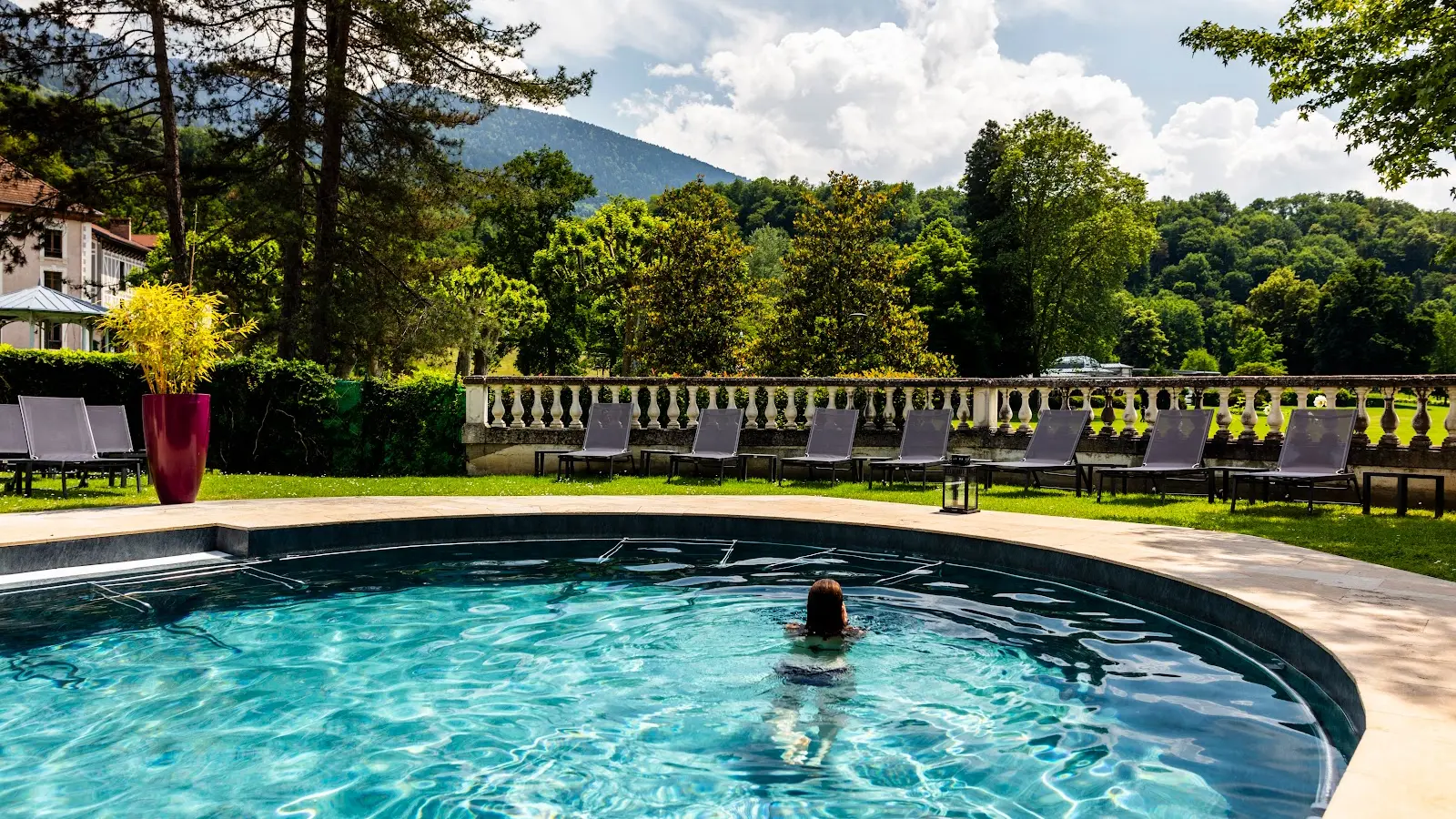 Une femme nage dans la partie extérieure de la piscine d’eau thermale avec sa vue sur le parc thermal.