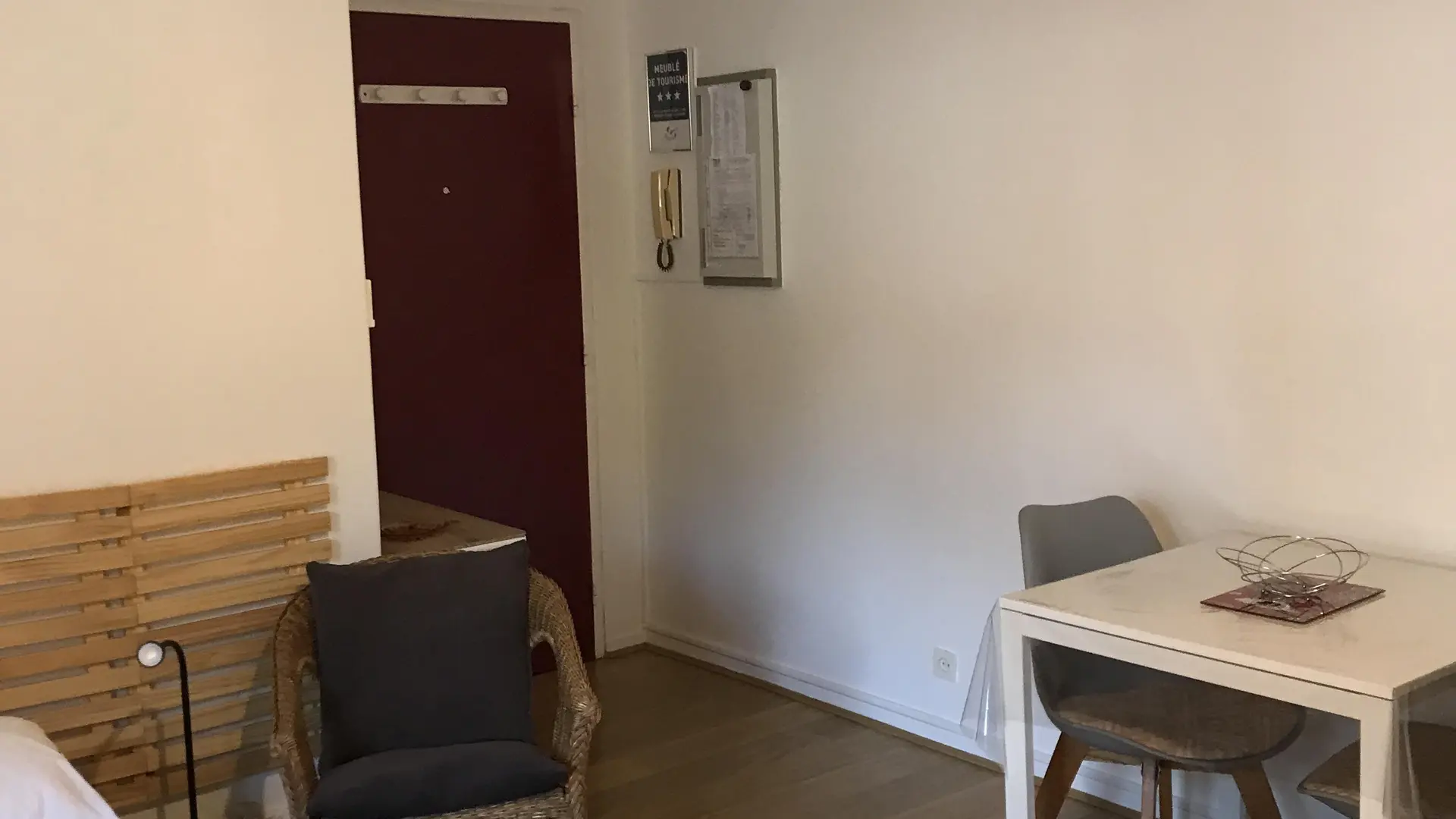 Un studio avec un sol en parquet, des murs clairs, un coin repas composé d'une petite table et de chaises, et un luminaire suspendu au plafond.