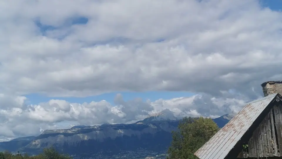 L'image montre un chalet en bois situé en montagne. Le toit est pentu et couvert de bardeaux.