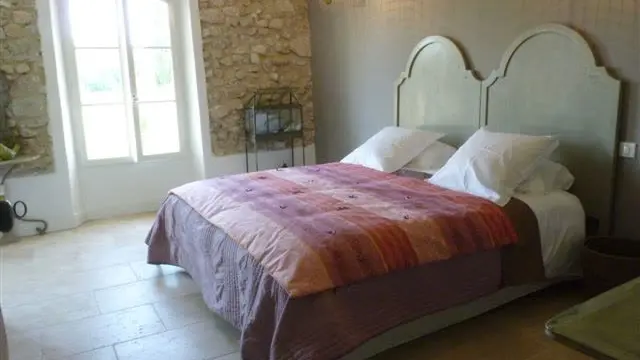 Chambre en pierre apparente, lit double aux tons prune et rose.