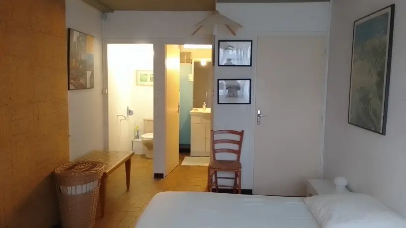 Chambre avec deux lits simples et une salle de bain avec un meuble vasque blanc et du carrelage bleu au fond.