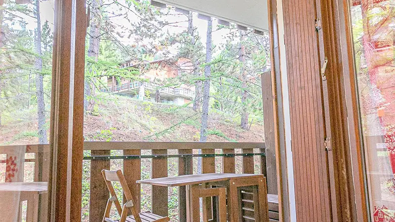 The studio's wooden terrace features an outdoor table and chairs, overlooking the greenery.