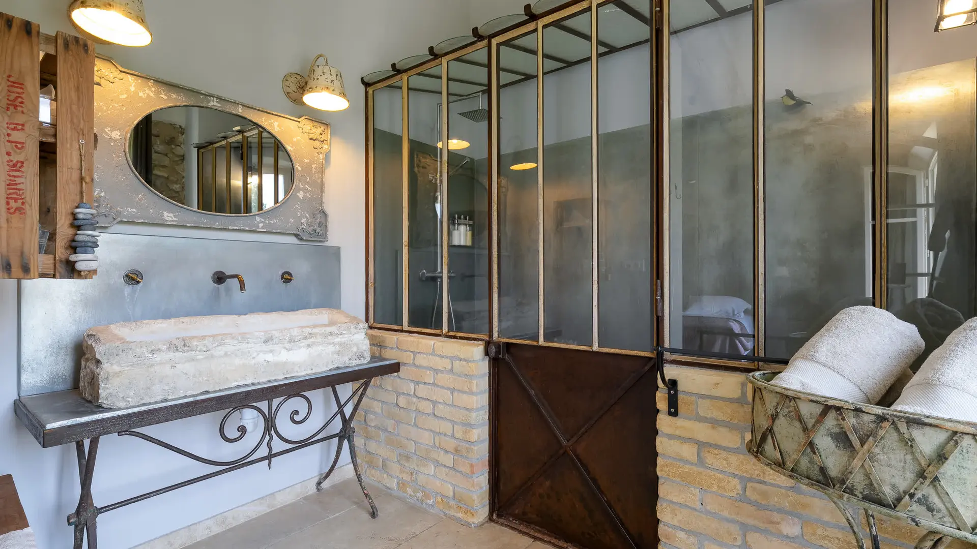 Salle de bain au style industriel et rustique : vasque en pierre, grande verrière et murs en brique.