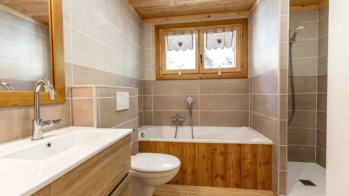 Salle de bains moderne et lumineuse avec baignoire, bac à douche, toilettes, ameublement bois, fenêtre