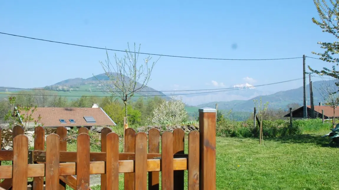 Un terrain herbeux, entouré d'une clôture en bois et l'on peut deviner un paysage montagneux à l'horizon.