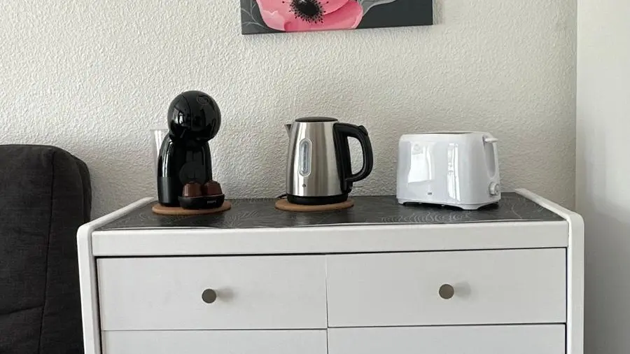 Un meuble de rangement avec un tiroir et deux portes surmonté d'une machine à café, d'un grille-pain et d'une bouilloire.