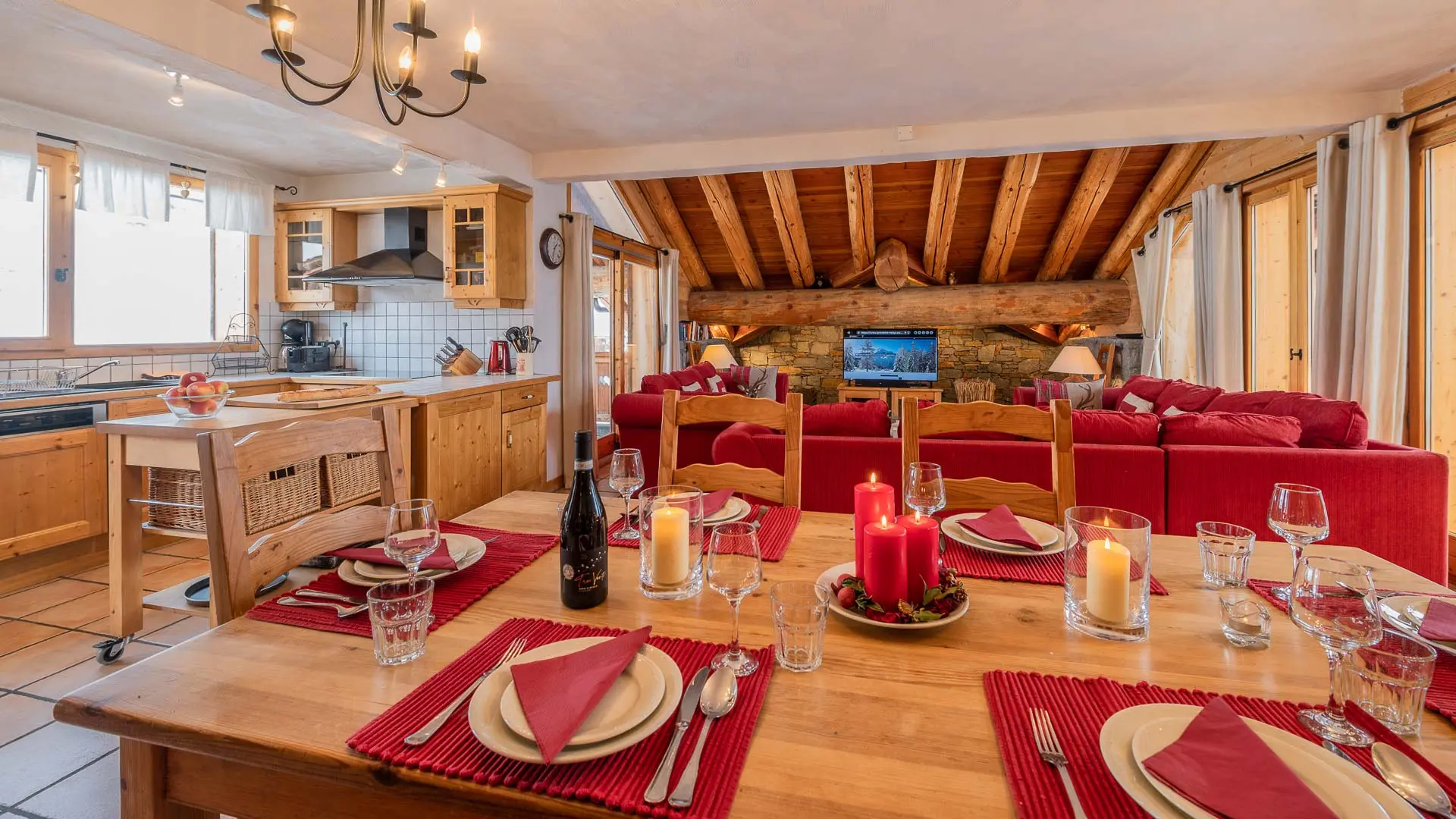 Grande table à manger dressée pour 8 personnes, coin cuisine entièrement équipée, salon sur le fond avec canapés d'angle et TV