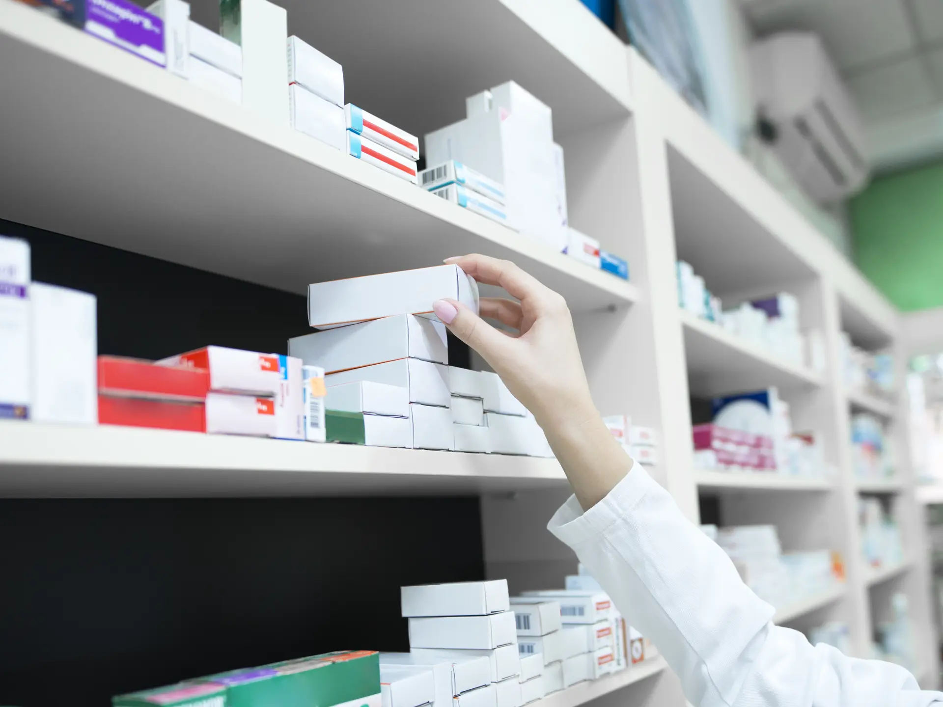 Closeup view of pharmacist hand taking medicine box from the shelf in drug store.