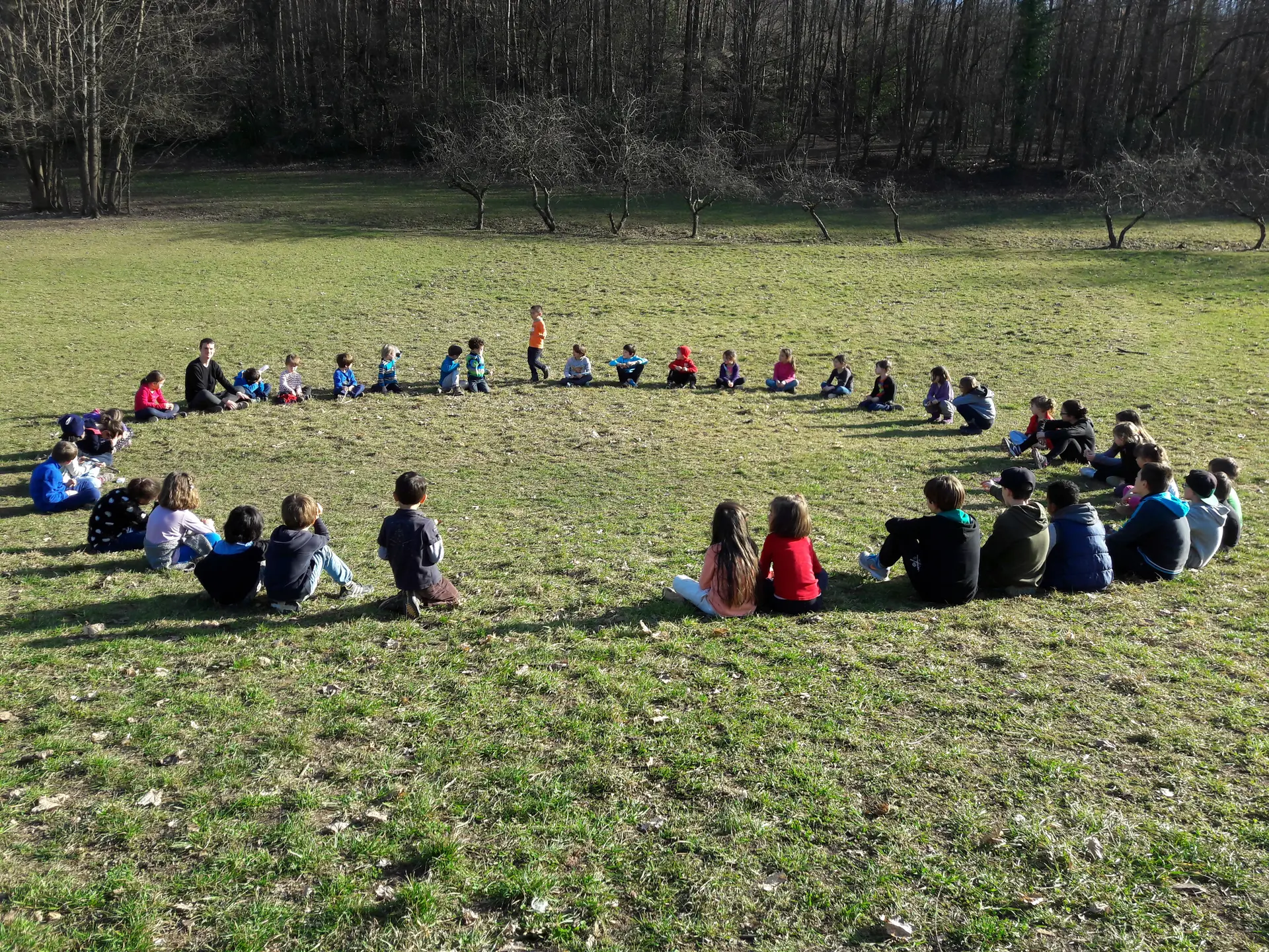 Un grand cercle d'enfants assis dans une prairie.