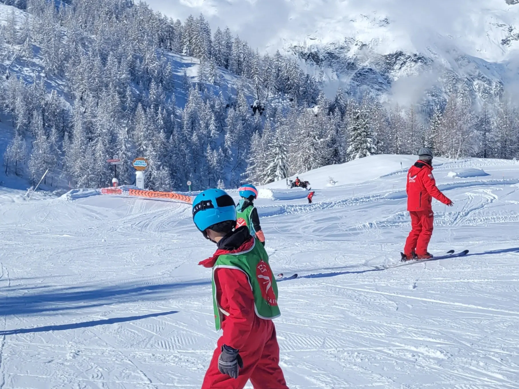 Un enfant au 1er plan qui skie, un moniteur ESF derrière