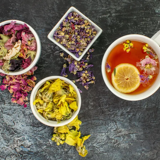 close up photo of herbal tea near bowls of dry flowers on grey background