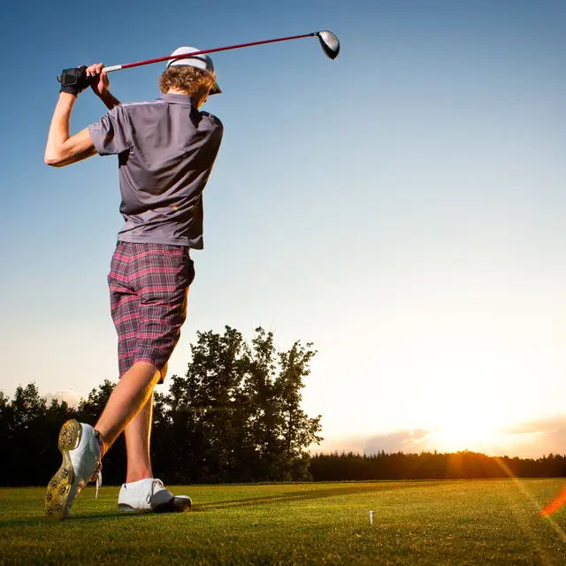 Male golf player teeing off golf ball from tee box to beautiful sunset