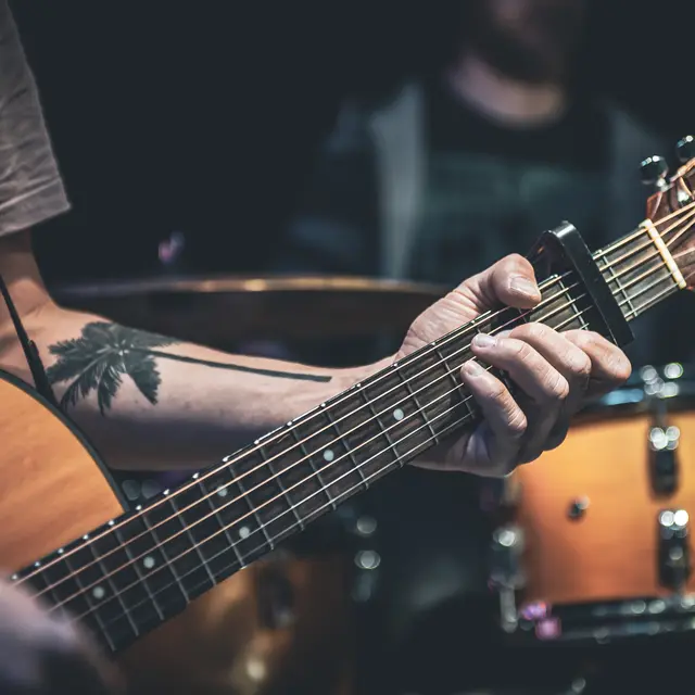 A man plays an acoustic guitar in the dark, close-up.