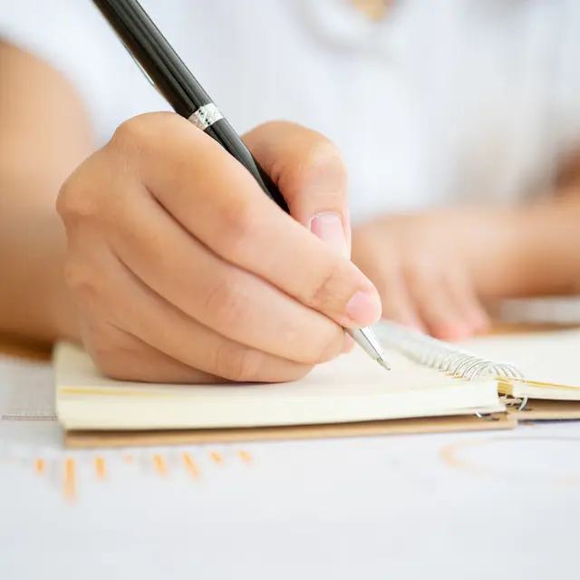Close shot of businesswoman hands holding a pen writing something on the paper on the foreground in office. Recording concept