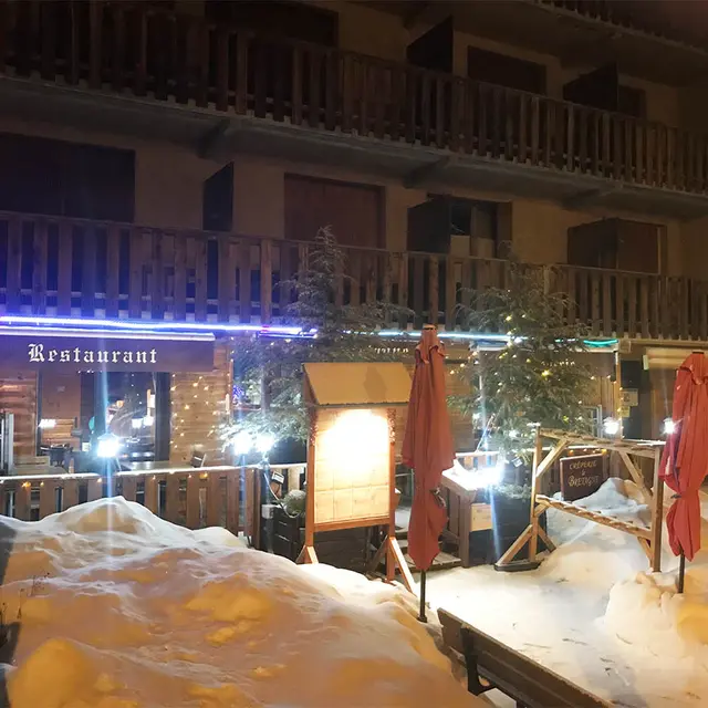 Vue nocturne de la façade de la crêperie, située en RDC, sapins en décoration sur la terrasse, neige