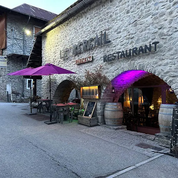 Restaurant, situé dans une bâtisse en pierre avec entrée accessible par une voûte en plein cintre. Terrasse extérieure, tonneaux en décoration. Ecriteau Le Bercail Pizza Restaurant