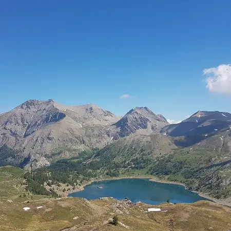 Lac d'Allos visible depuis le Col de l'Encombrette, grande étendue d'eau entourée de montagnes et de végétation