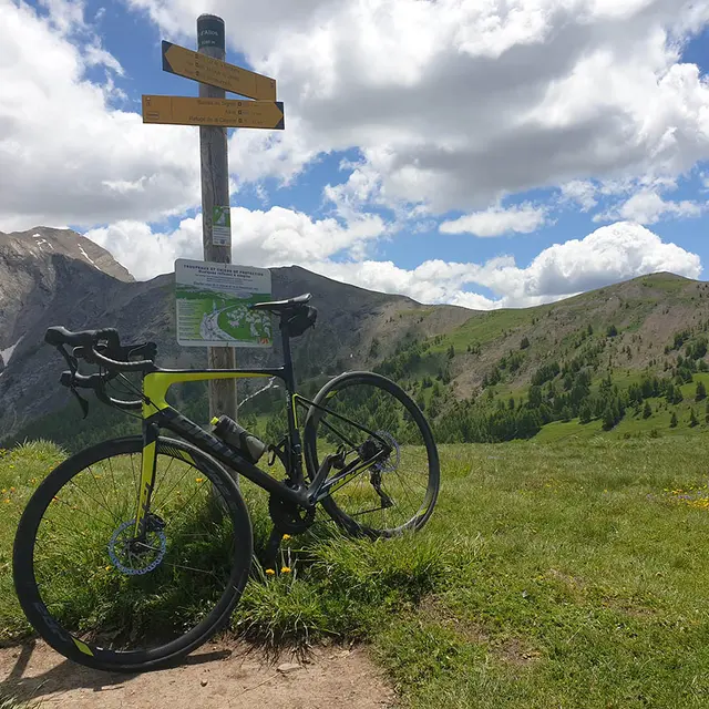 VTT appuyé contre un panneau de randonnée situé au Col d'Allos, sommet des montagnes visibles tout autour