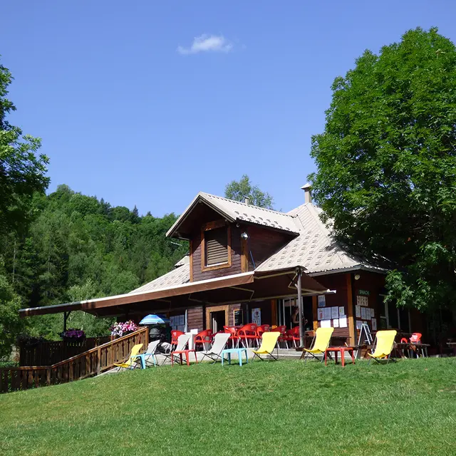 Vue d'ensemble du restaurant du Parc de Loisirs, bâtiment en bois sur 2 étages avec terrasse (tables, chaises, chaises longues), dans un cadre forestier