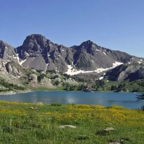 Le lac d'Allos au mois de juillet, nombreuses fleurs encore présentes et des névés résiduels au pied des Tours du lac.