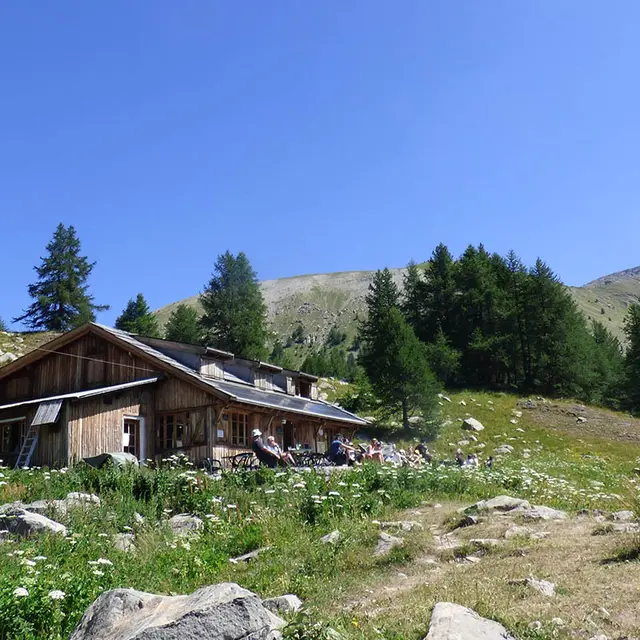 Vue du refuge-restaurant, maison en bois au milieu de la végétation, terrasse, tables et chaises