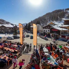 Terrasse de la brasserie avec une grande foule, tables et chaises, située à côté de la place centrale de la Foux, vision sur la station