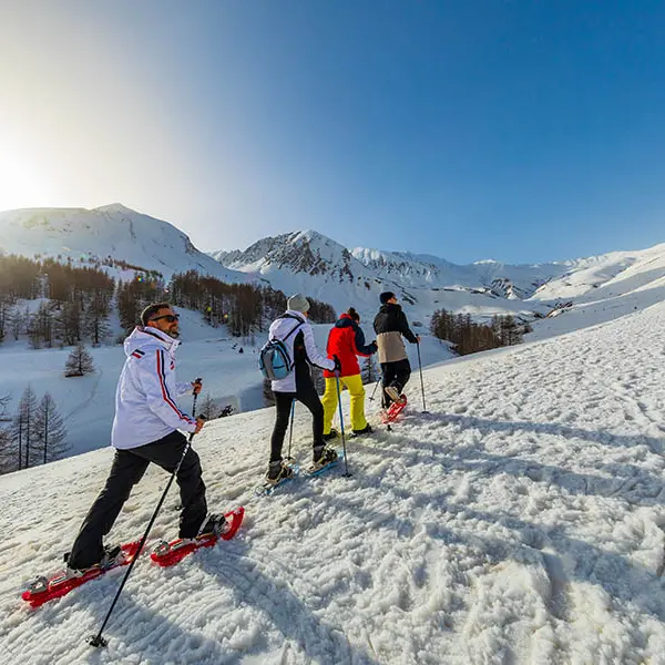 Randonneurs en raquettes montant le long du sentier de la cabane de Sestrière, cirque dégagé ensoleillé avec montagnes enneigées