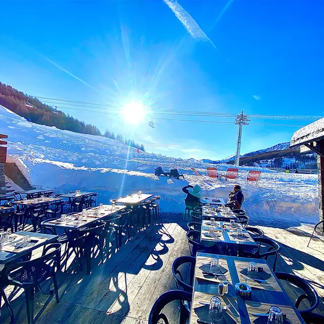 Terrasse ensoleillée du restaurant, tables et chaises, accès aux pistes enneigées, télésiège à proximité