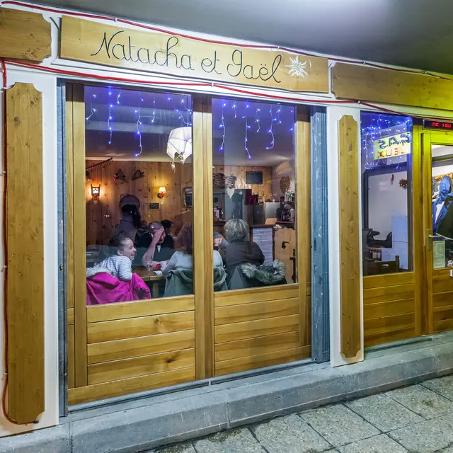 Vitrine du restaurant, façade en bois avec inscription gravée Natacha et Gaël. A l'intérieure table et chaises, ambiance confortable