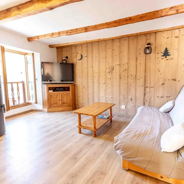 Séjour moderne et lumineux avec canapé, table basse, TV, poêle à bois, porte-fenêtre, ameublement bois et parquet au sol