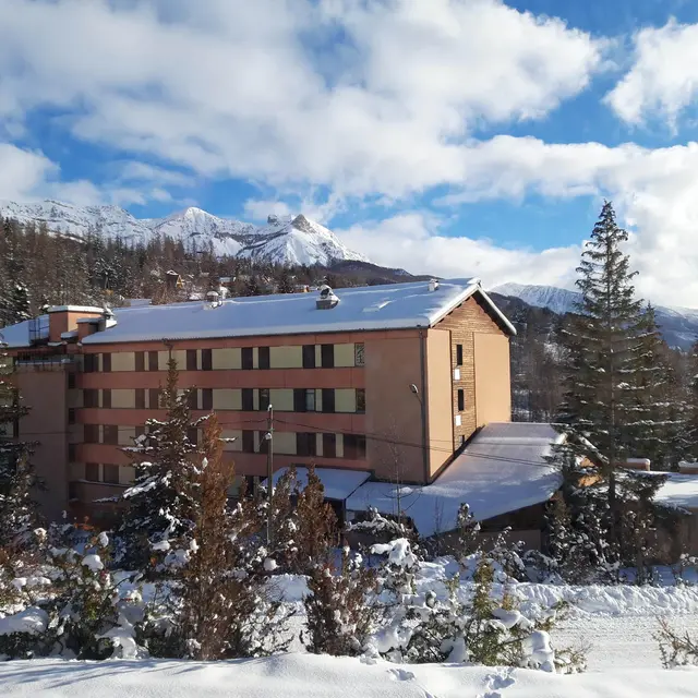Vue extérieur du centre de vacances, bâtiment sur plusieurs étages au milieu des montagnes enneigées